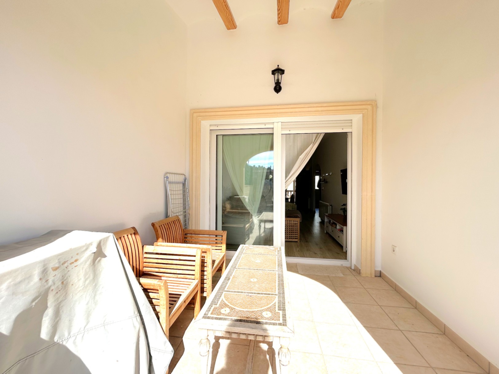 Covered terrace featuring exposed wooden ceiling beams, ceramic tiling, and a mosaic table. Large sliding doors provide seamless access to the interior.