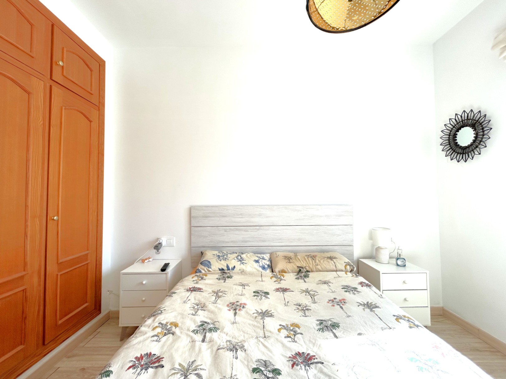 Double bedroom featuring a built-in wooden wardrobe, white bedside tables, and a light wood headboard. The room includes laminate flooring and bright natural lighting.