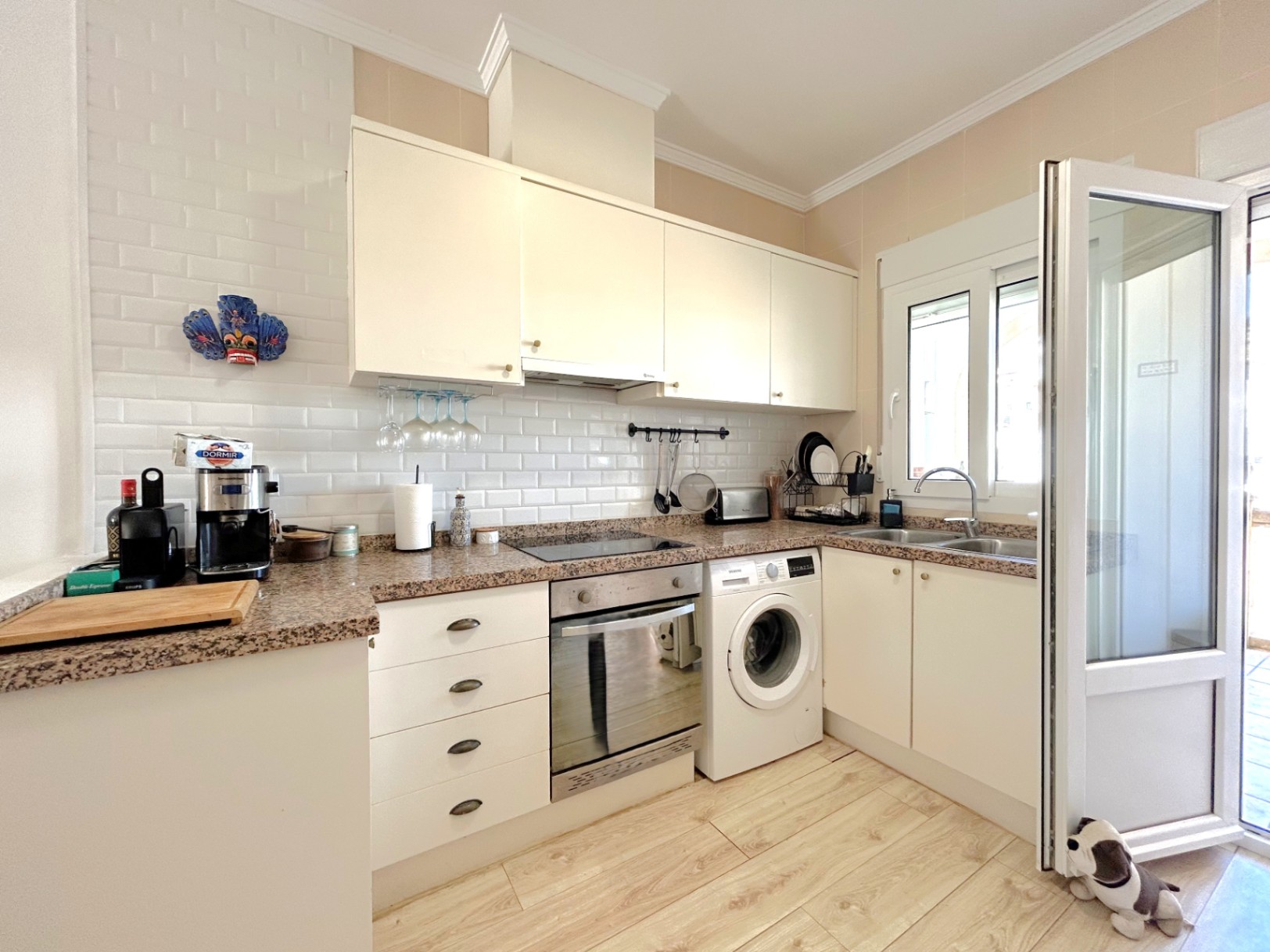 Equipped kitchen featuring granite countertops, white cabinetry, and a subway tile backsplash. It includes integrated appliances and wood-effect ceramic flooring.