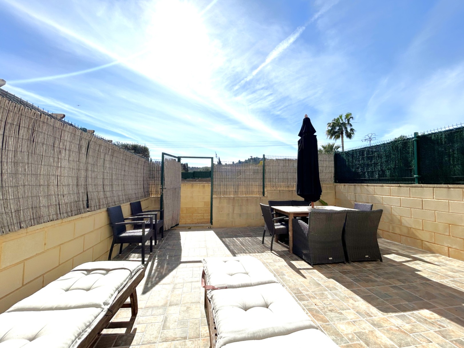 South-facing private terrace featuring stone-effect tiling, a complete outdoor dining set with parasol, and comfortable sun loungers under natural light.