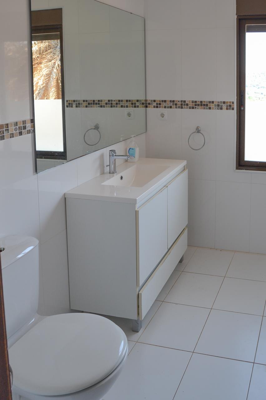 Bathroom featuring a white vanity unit, large frameless mirror, and tiled walls with a decorative mosaic border. Natural light enters through the side window.