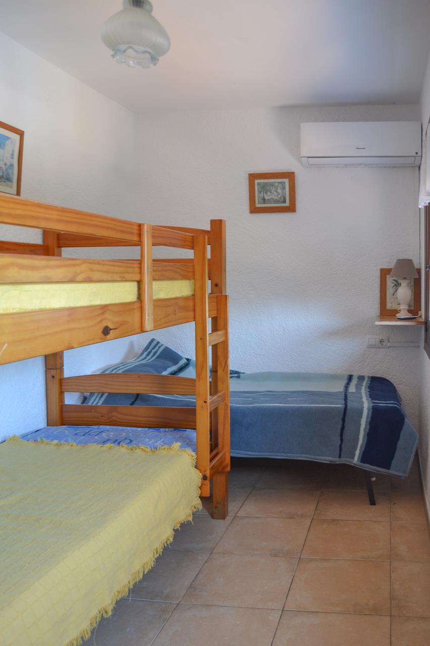 Bedroom featuring pine wood bunk beds and a single bed, complete with wall-mounted air conditioning, ceramic tile flooring, and textured white walls.