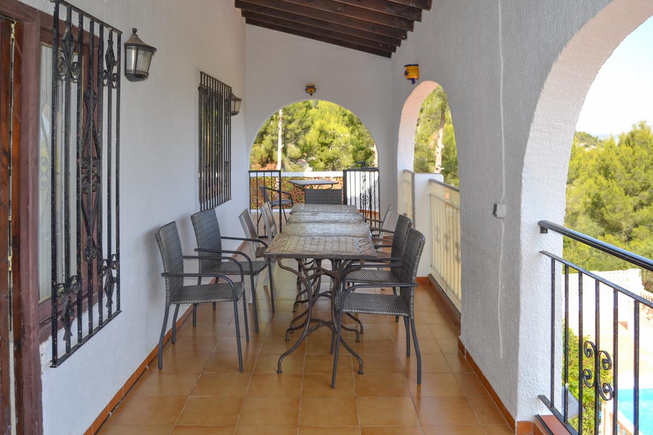 Covered naya featuring traditional arches, dark wood beams, and terracotta flooring. The space includes an outdoor dining area overlooking the surrounding pine forest.