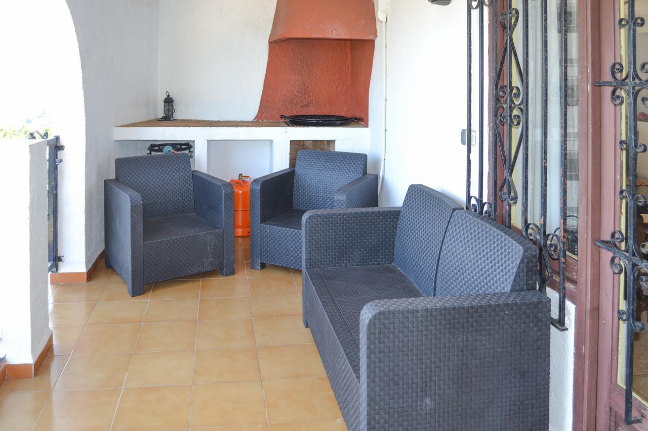 Covered terrace area featuring dark wicker-style seating, terracotta floor tiles, and a built-in barbecue with a traditional clay-colored chimney.