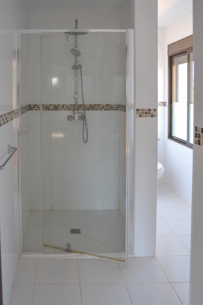 Functional bathroom featuring a walk-in glass shower, white tiling with earth-toned mosaic accents, and natural light from the adjacent window.