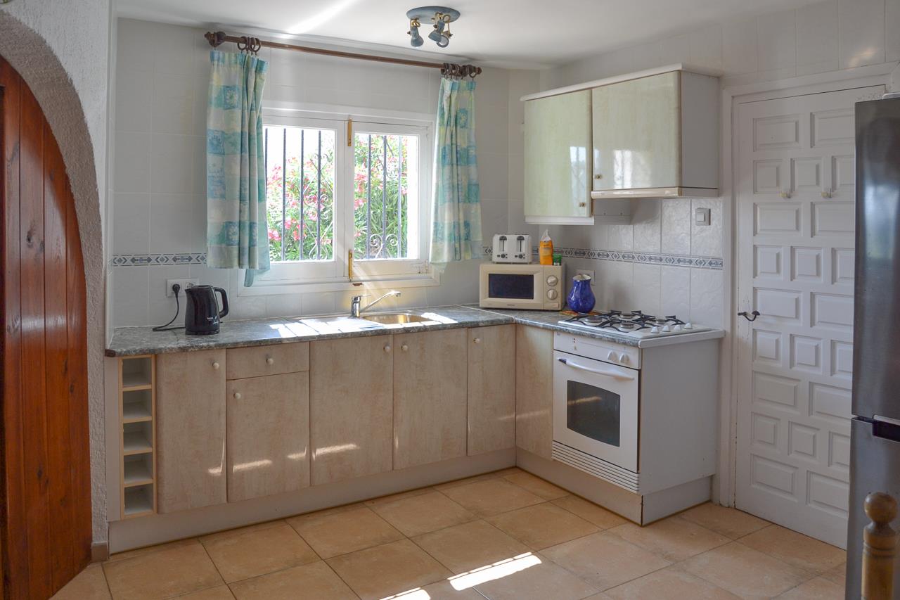 Functional kitchen featuring cream cabinetry, granite-effect countertops, and essential appliances including a white oven and gas hob, lit by natural light.