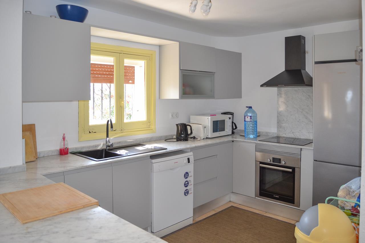 Functional kitchen featuring grey cabinetry, marble-effect countertops, and stainless steel appliances. A yellow-framed window provides natural light over the integrated sink.