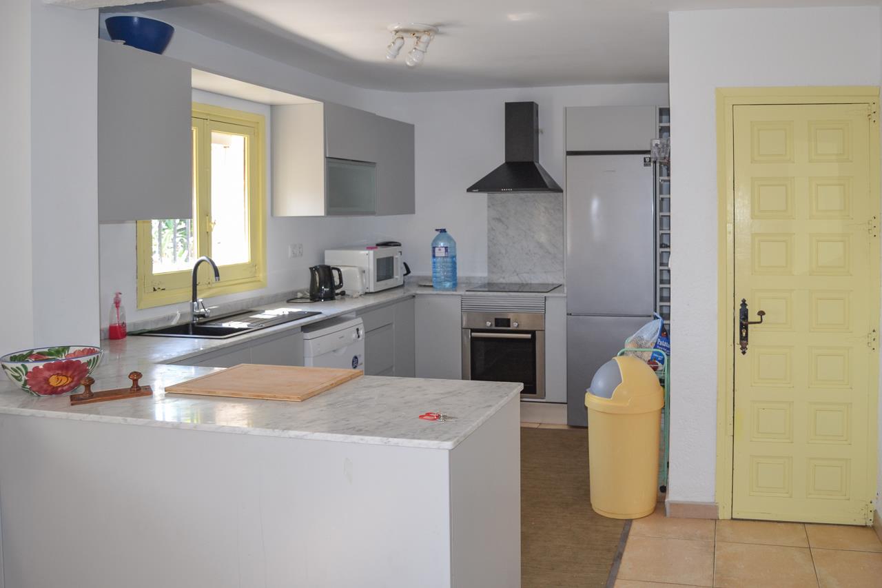 Functional kitchen featuring marble countertops, soft grey cabinetry, and integrated appliances. The space is accented by a yellow window frame and matching door.