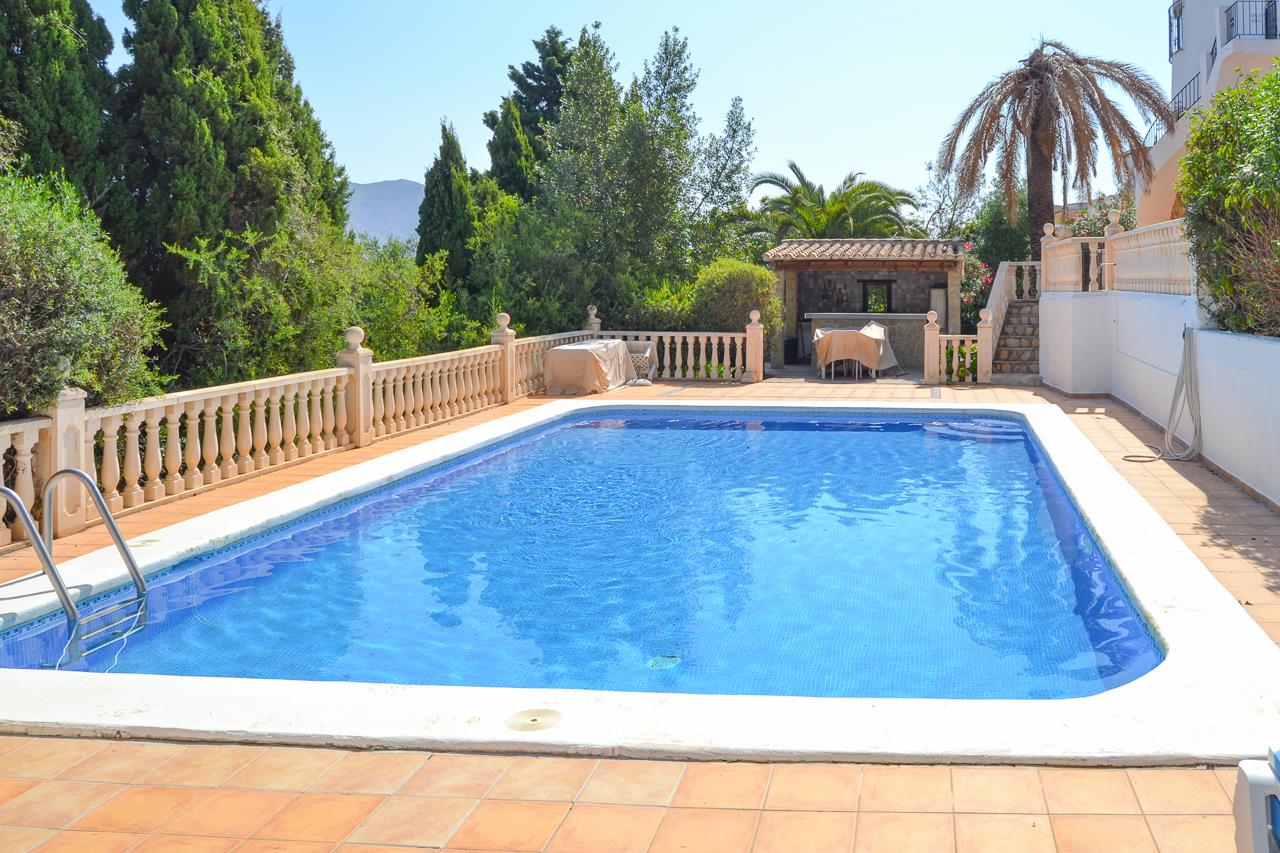 Large 12x6 meter swimming pool with blue mosaic tiling, featuring a terracotta terrace with stone balustrades and a covered outdoor bar area set against lush greenery.
