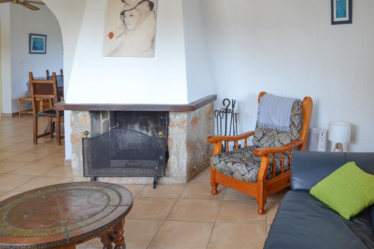 Living area featuring a stone fireplace with a wooden mantel, rustic seating, and tiled floors. An archway provides a seamless transition to the dining space.
