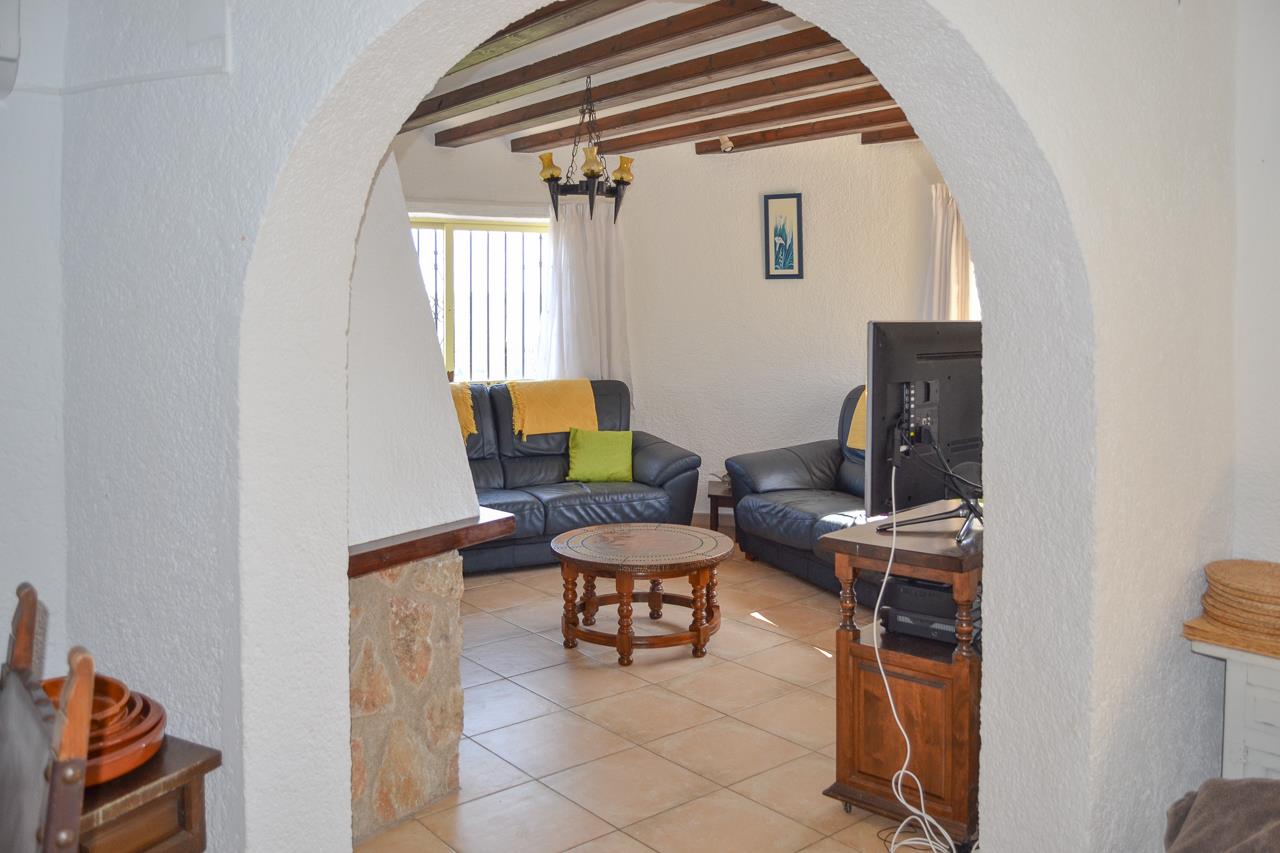Living area with exposed wooden ceiling beams and leather sofas, framed by a white archway. Features tiled flooring and a rustic stone-clad wall section.