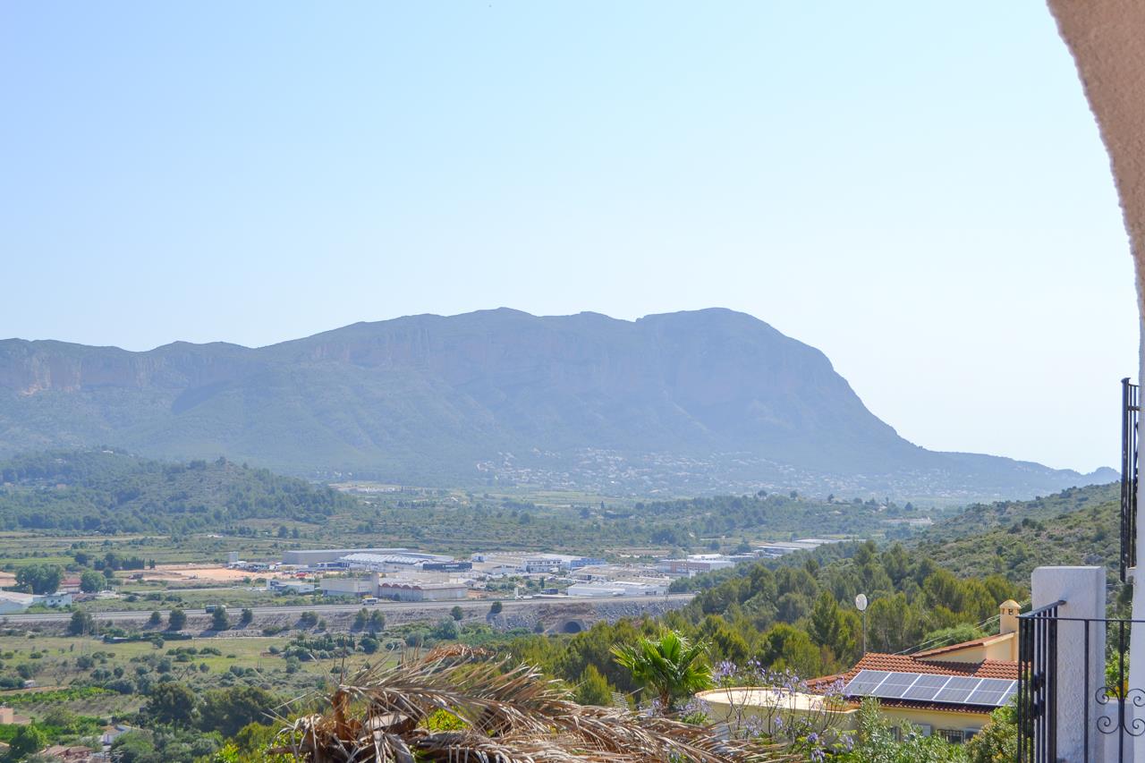 Panoramic open views of the valley and mountain range from the terrace. The landscape features lush Mediterranean greenery and a clear horizon under bright daylight.