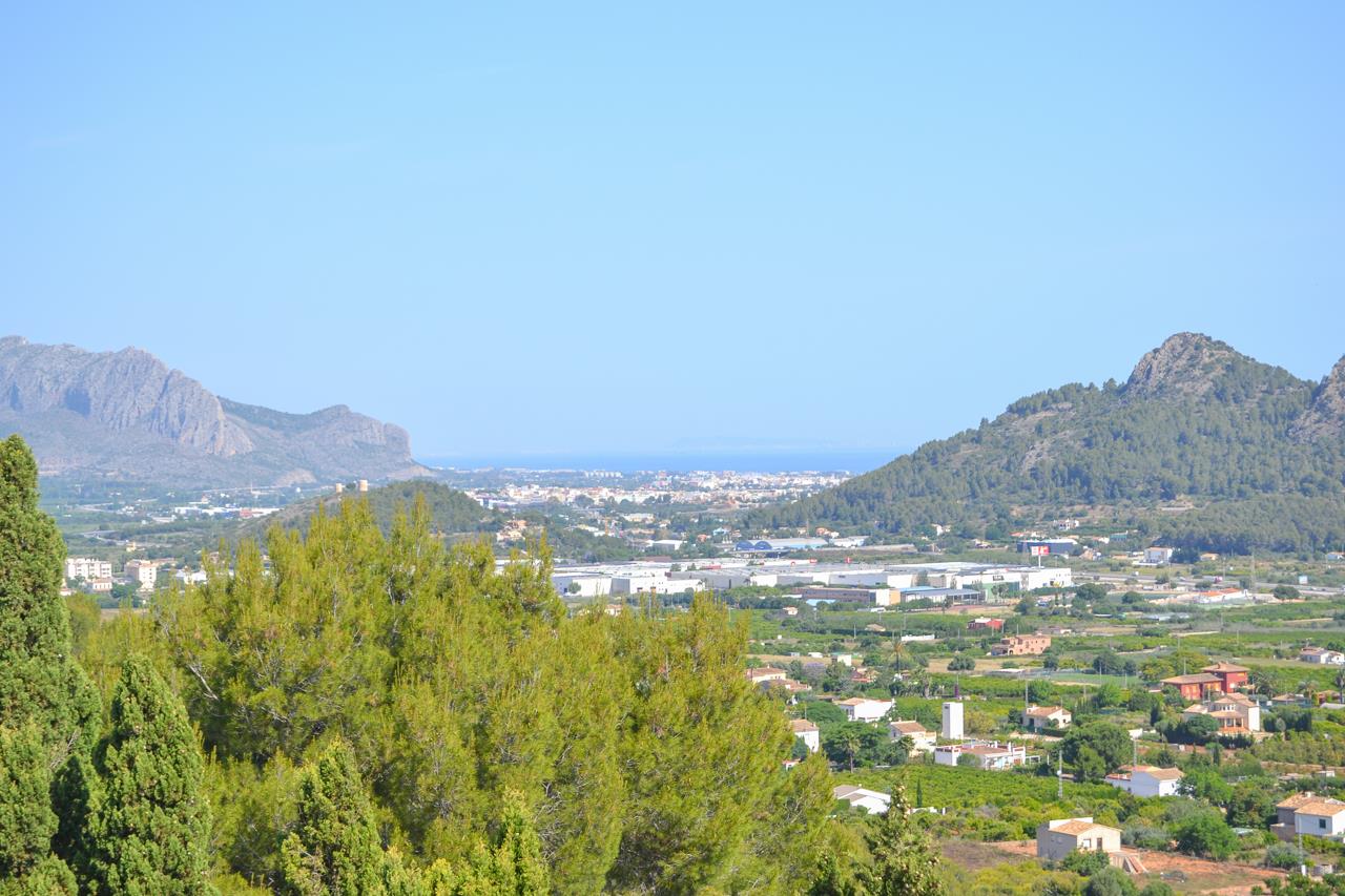 Panoramic open views overlooking the valley and the Mediterranean Sea, framed by mountain ranges and lush pine trees under a clear blue sky.
