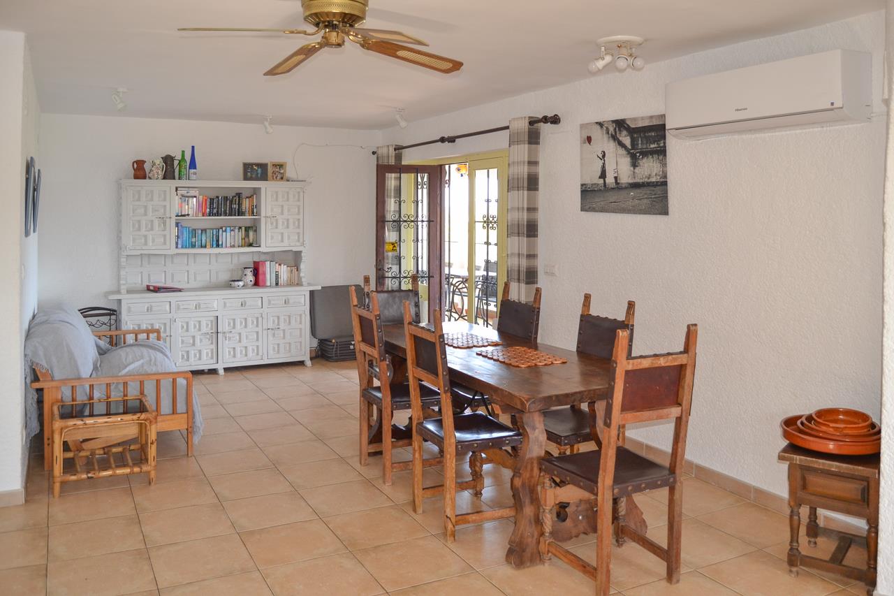 Rustic dining area featuring a solid wood table, high-back chairs, and a white hutch. Includes a ceiling fan, split-unit air conditioning, and access to the outdoor terrace.