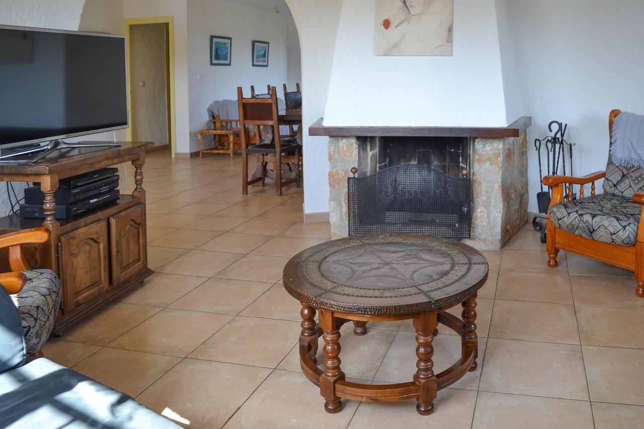 Rustic living area featuring a stone fireplace with a white chimney, ceramic tile flooring, and traditional wooden furniture under a Mediterranean archway.