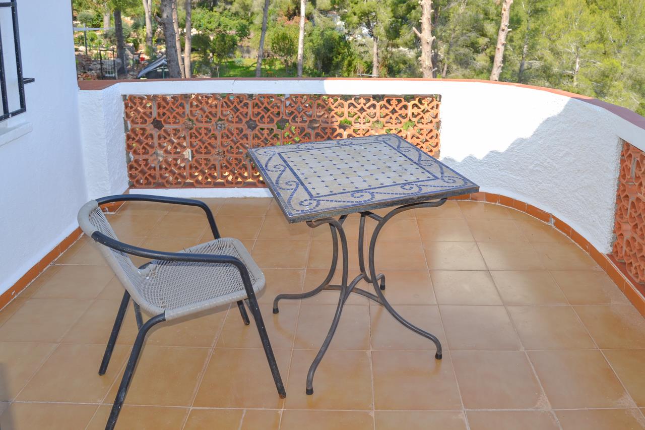 Terrace featuring terracotta tiling, a blue mosaic-top table, and a decorative ceramic lattice railing overlooking a lush pine forest.
