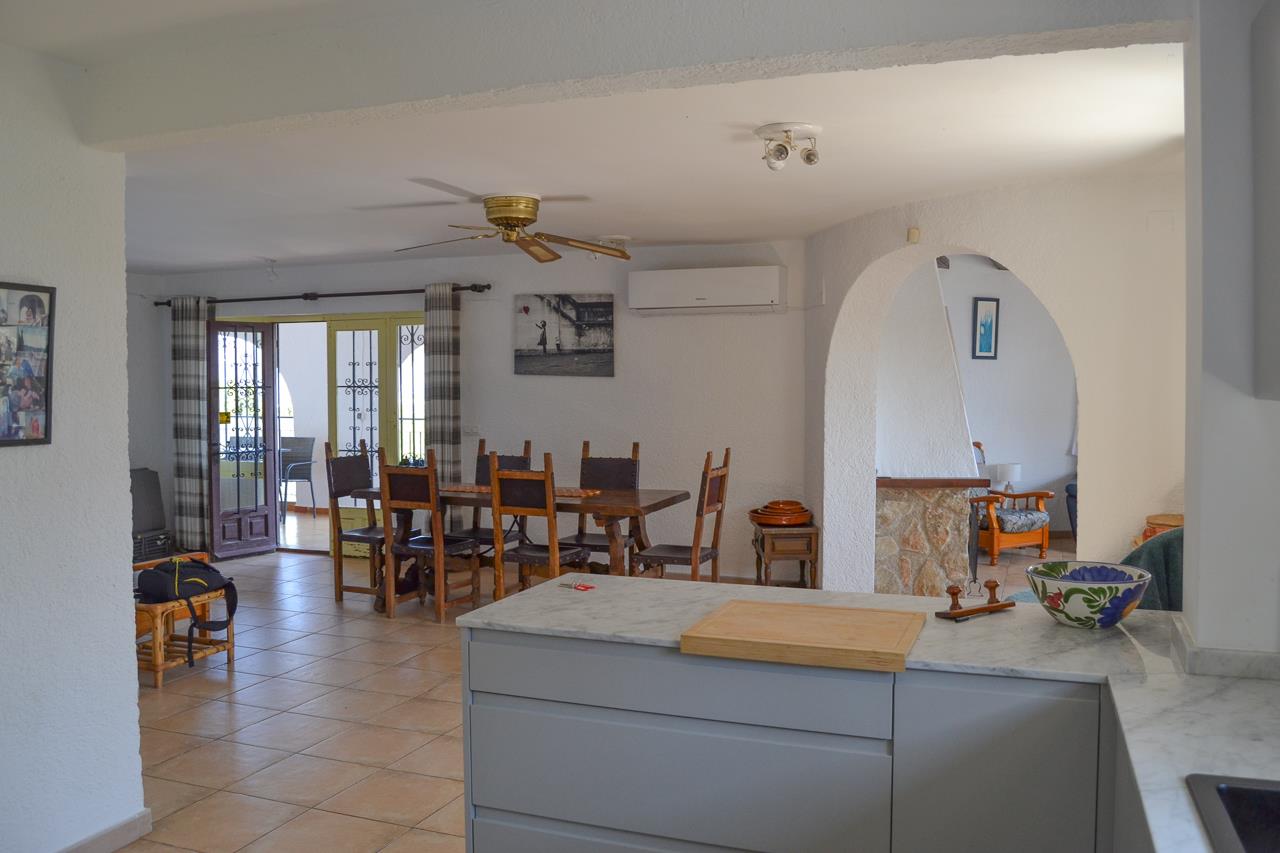 View from the open kitchen with marble countertops towards the dining area. Features tiled flooring, a ceiling fan, and direct access to the terrace through glass doors.