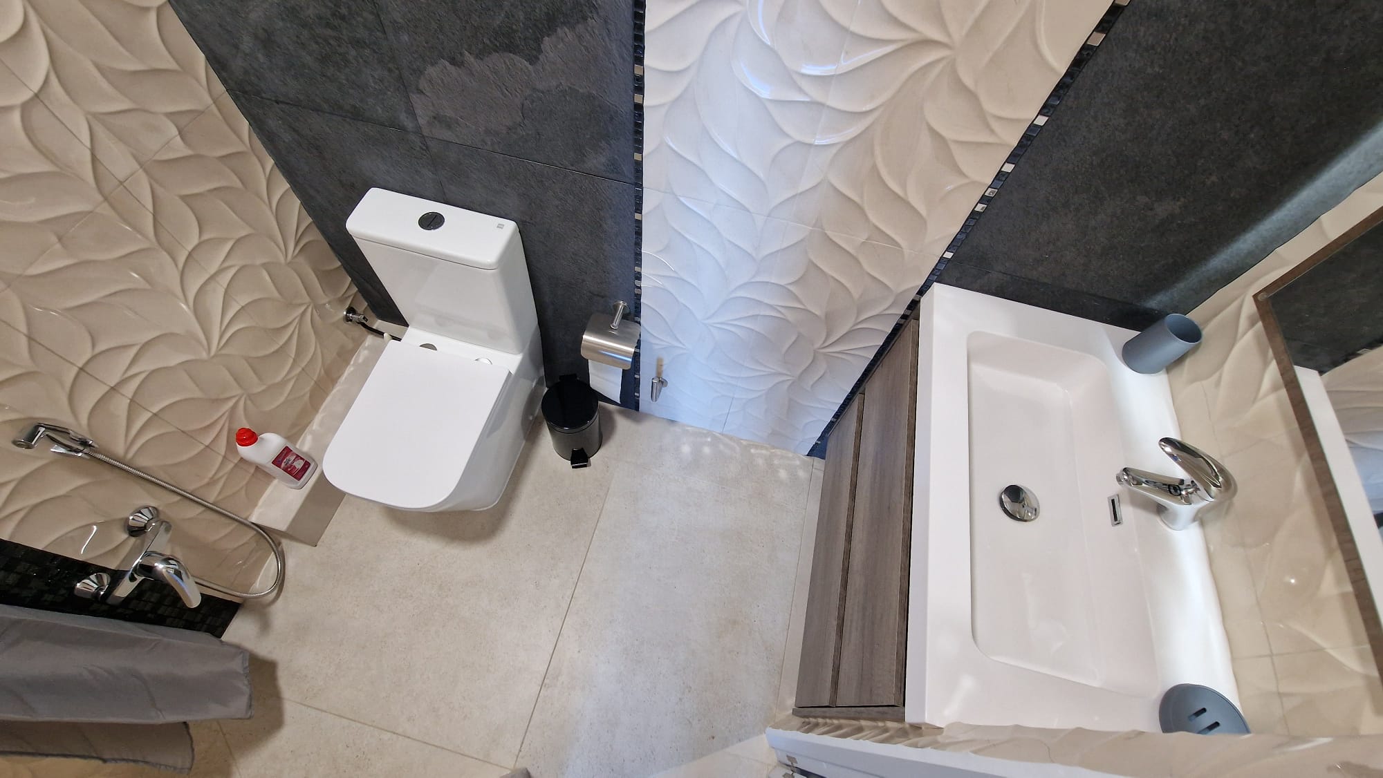 Bathroom detail featuring textured tiles, a white toilet, and a modern sink. Functional and elegant design.