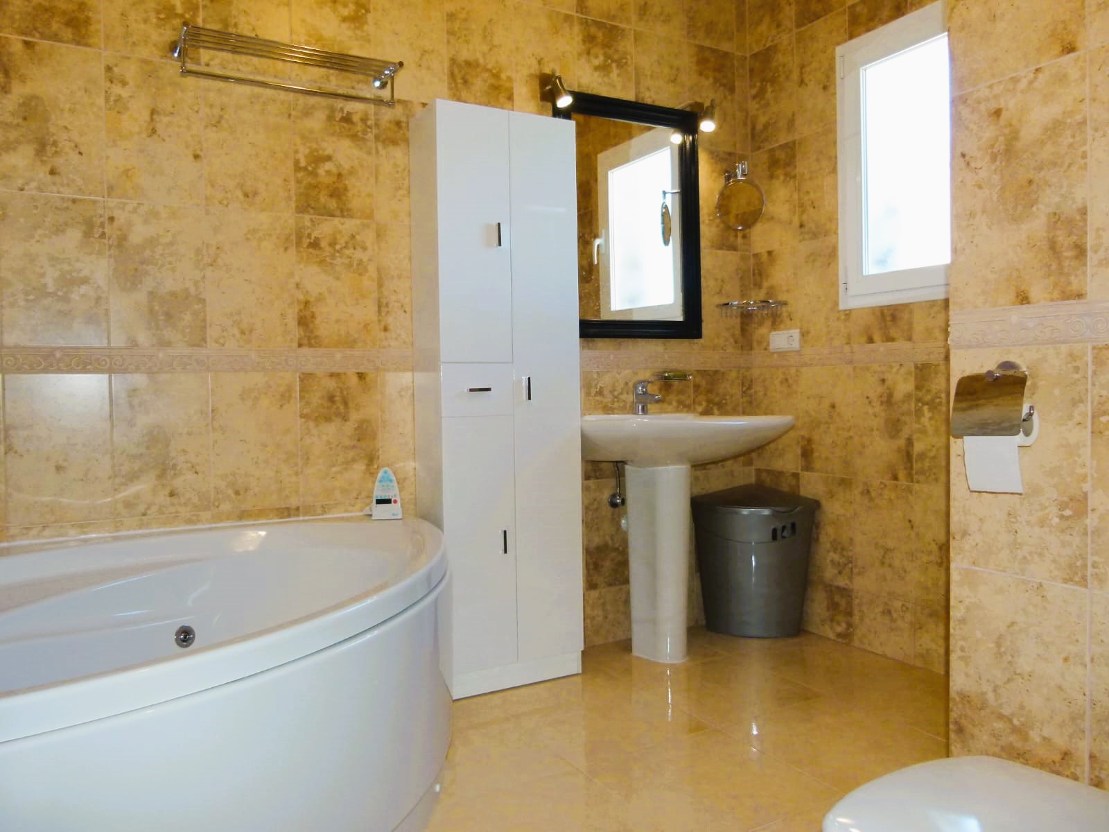 Bathroom featuring a round tub, pedestal sink, and beige-toned tiling.