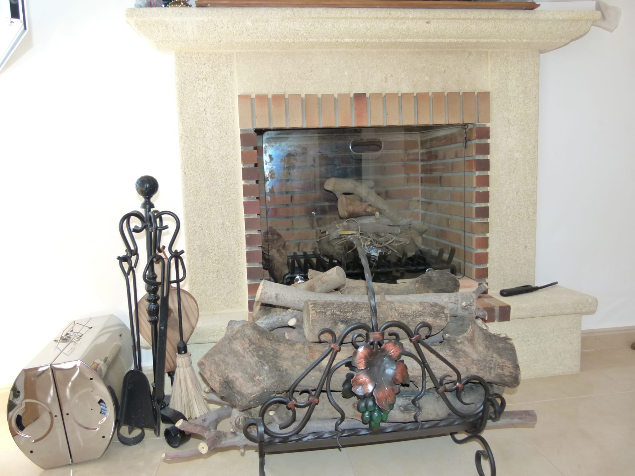 Brick fireplace with wrought iron tools and stacked firewood on a decorative stand.