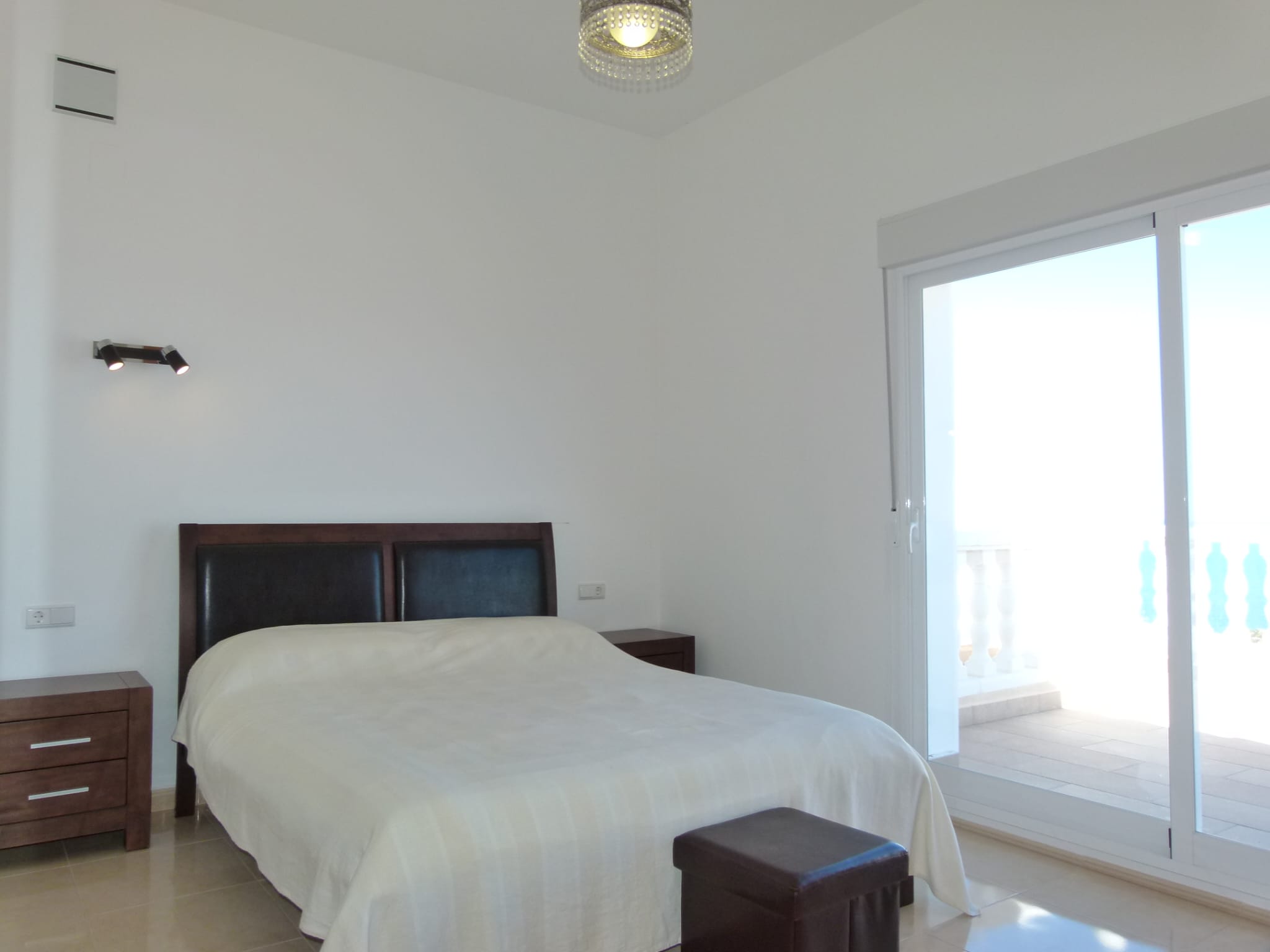 Bright bedroom featuring a double bed, dark wood nightstands, and access to a terrace with a white railing.