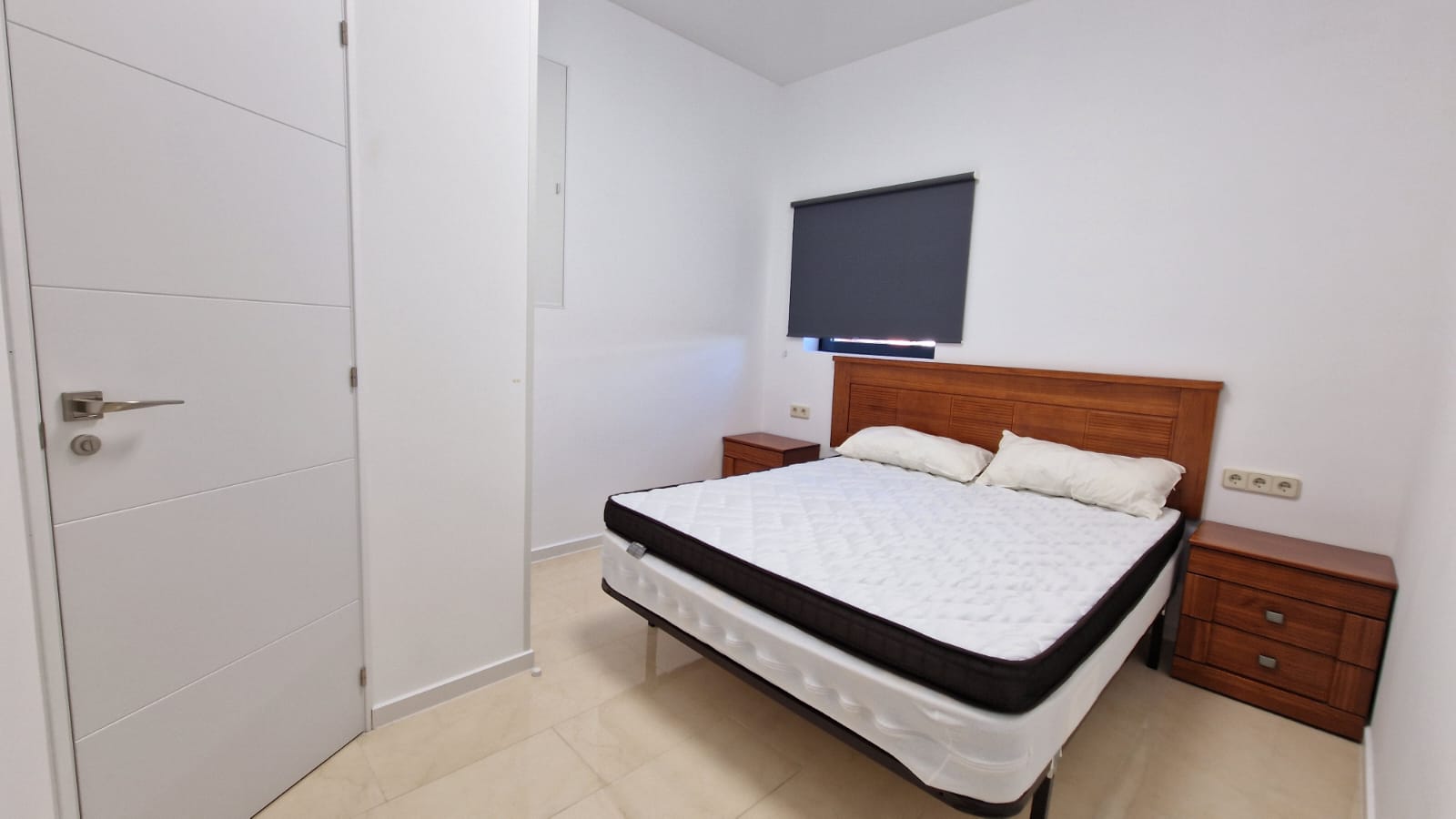 Bright bedroom featuring a double bed, wooden nightstands, and a modern white door.