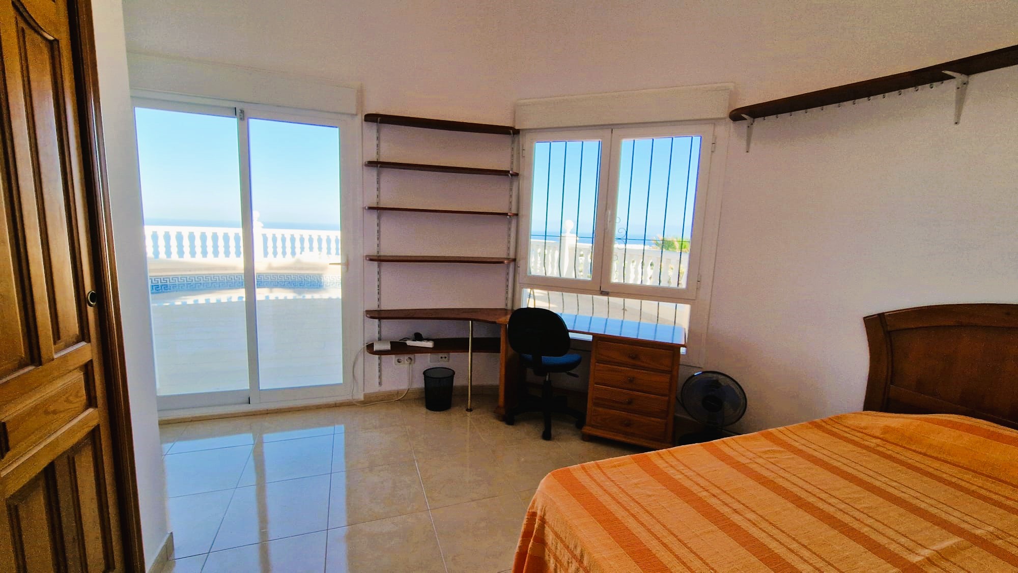 Bright bedroom featuring a wood desk, shelving, and views of the balcony with white railings.