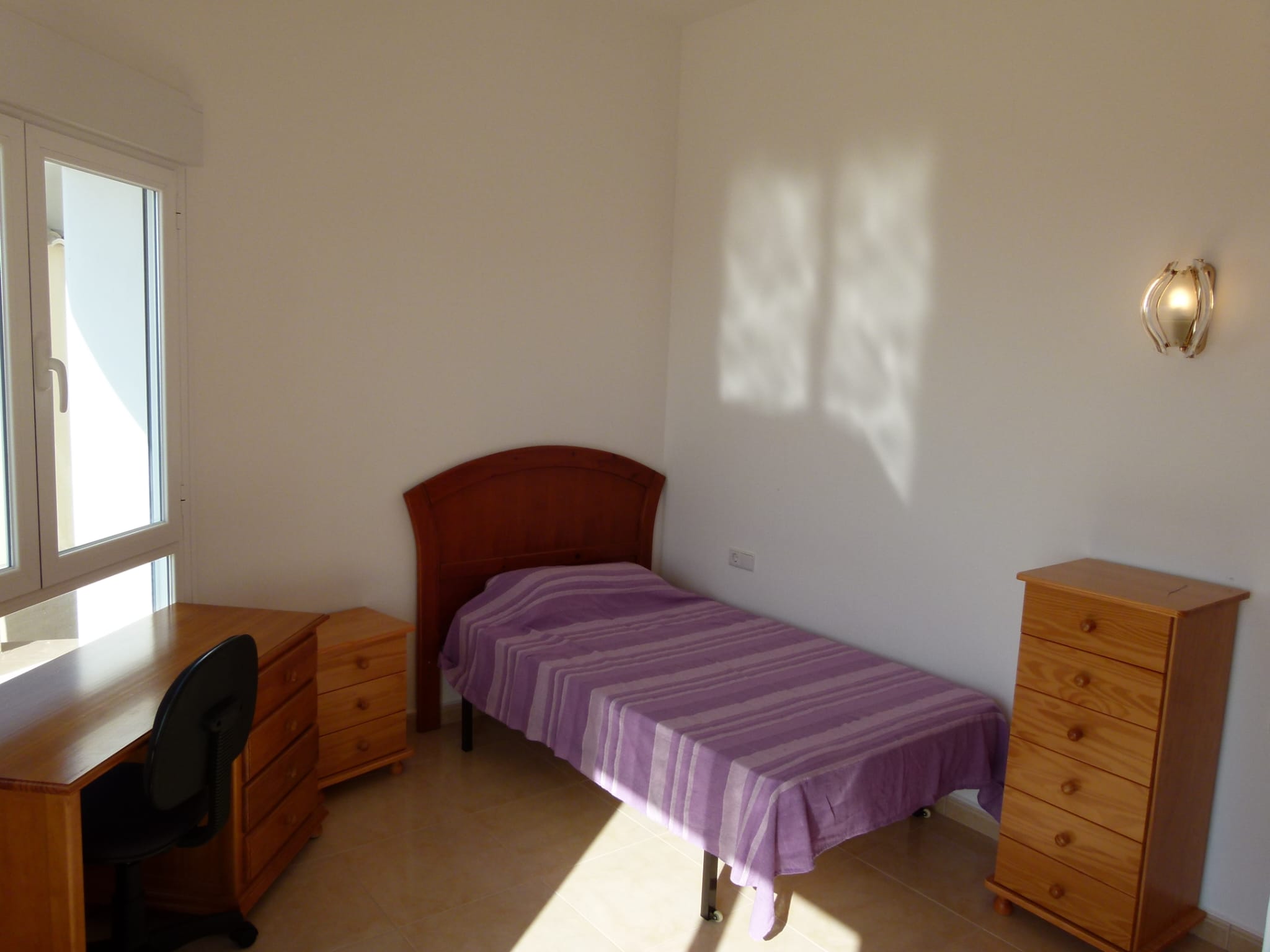 Bright bedroom with a single bed, wooden desk, and matching chest of drawers.