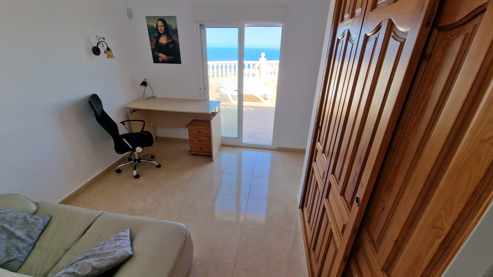 Bright room with a desk, wooden wardrobe, and terrace access with sea views.