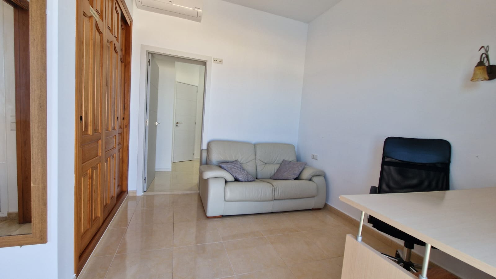 Bright room with wooden wardrobe, leather sofa and desk with office chair.