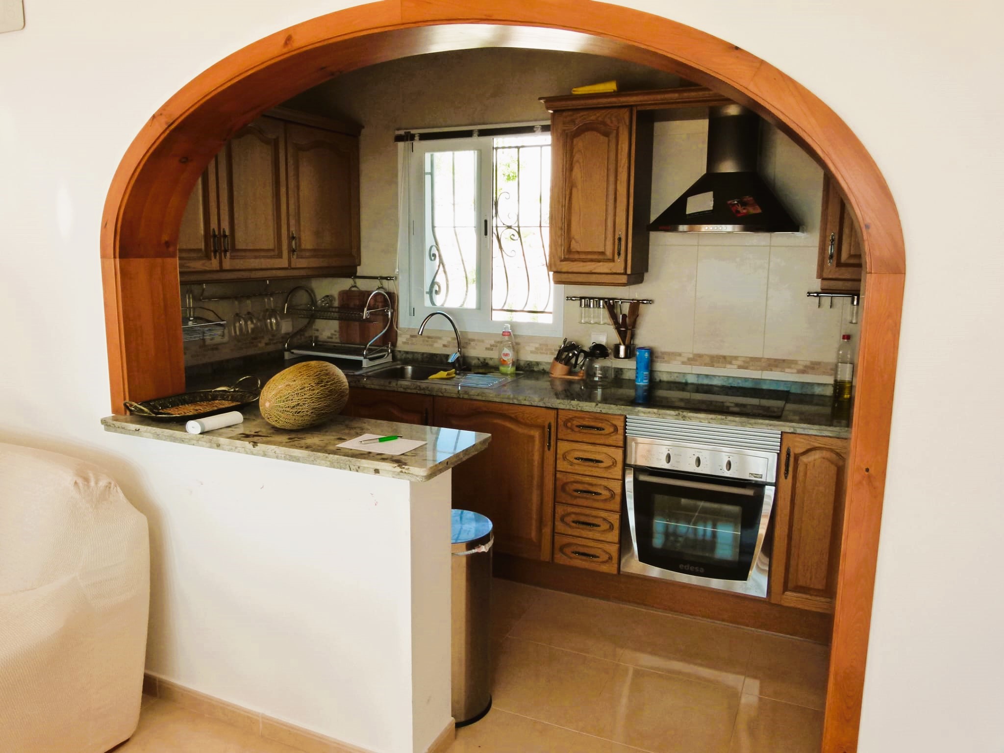 Kitchen with a wooden arch, honey-colored cabinets, and granite countertops. Rustic and functional style.