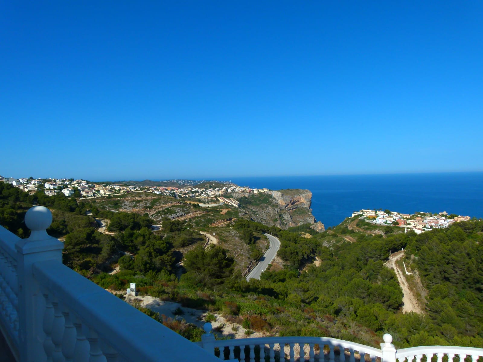 Panoramic views from the terrace with a white railing towards the coast and the blue sea.