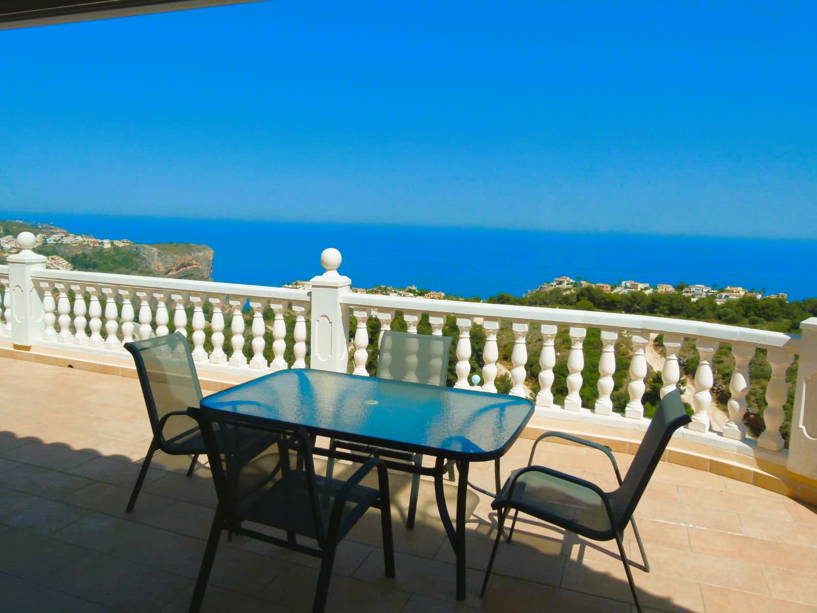 Terrace with glass table & sea view in Cumbre del Sol. White balustrade railing.