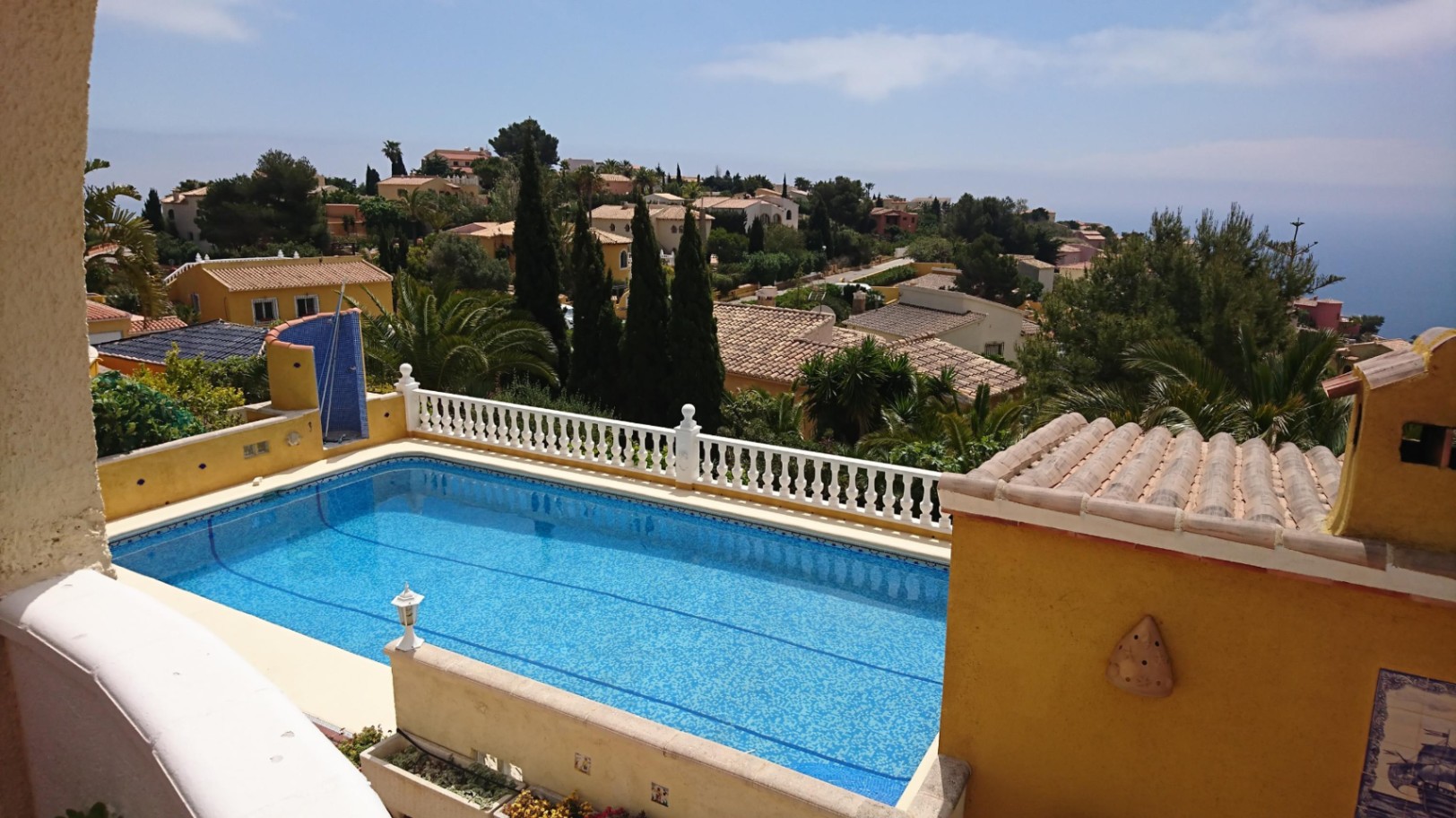 A 10x4 rectangular swimming pool with blue mosaic tiling, featuring a white balustrade and elevated views of the Mediterranean coastline and surrounding villas.