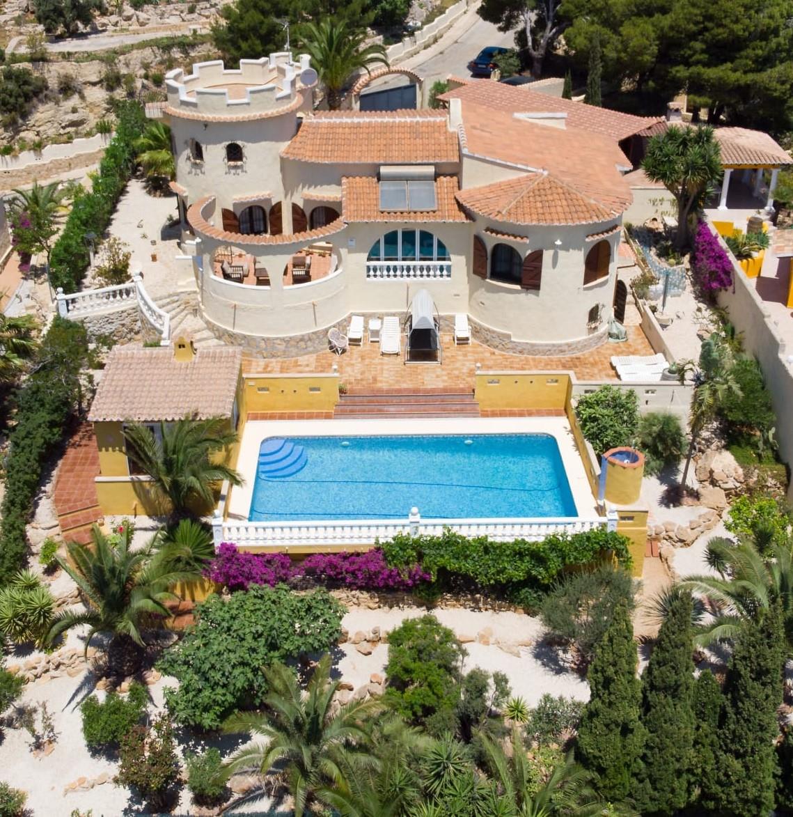 Aerial view of the Mediterranean villa featuring a distinctive tower, a 10x4m swimming pool with sun terrace, and a mature garden with palm trees.