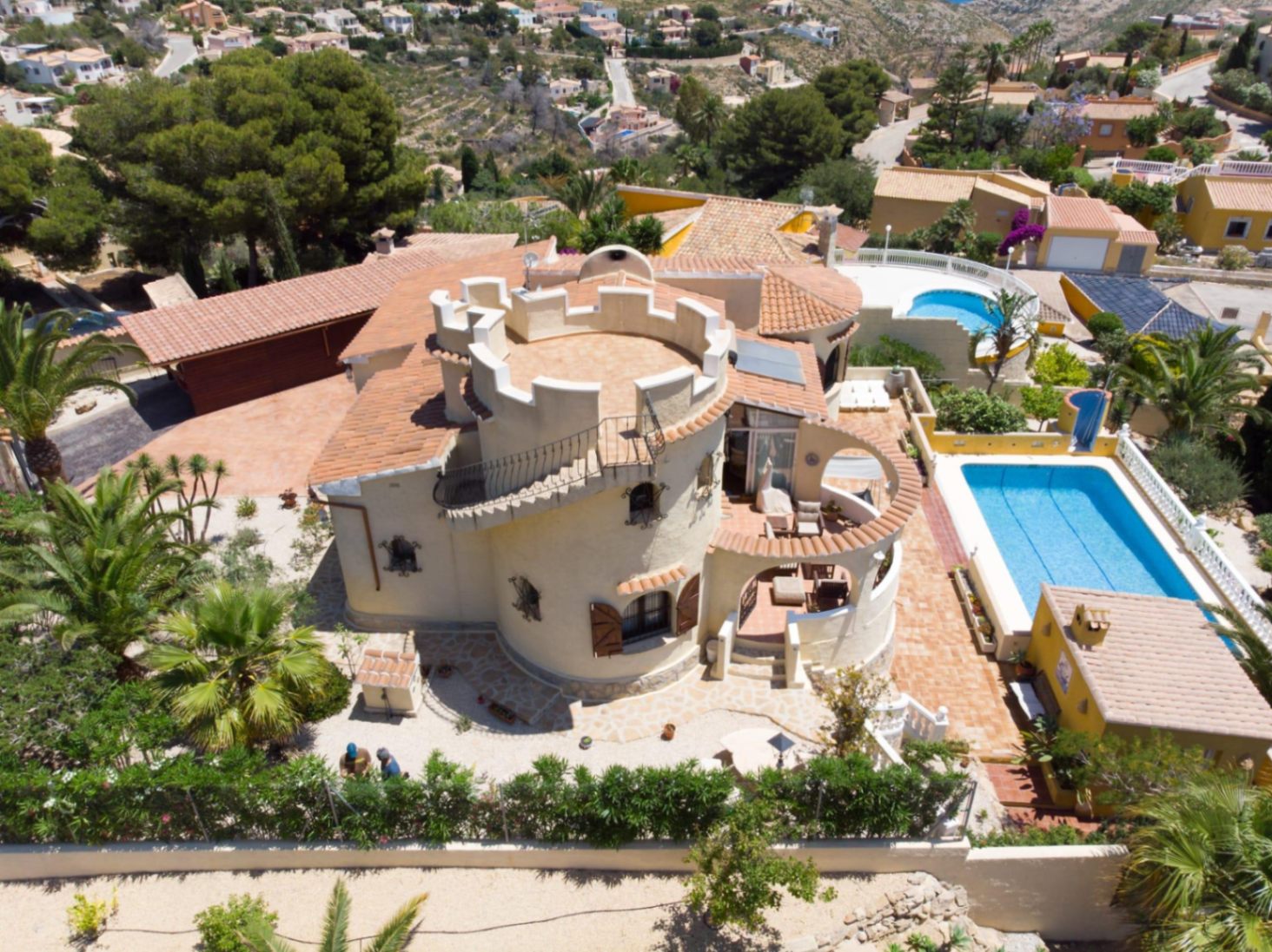Aerial view of the villa featuring a circular tower with a crenellated rooftop, a rectangular swimming pool, and an outdoor kitchen area set within landscaped gardens.