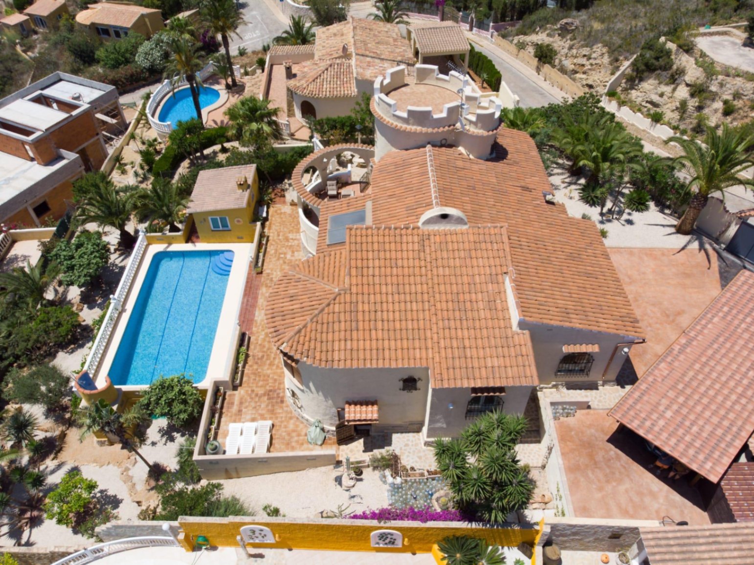 Aerial view showing the terracotta tiled roof, a unique white tower, a 10x4 meter swimming pool, and landscaped Mediterranean gardens with palm trees.