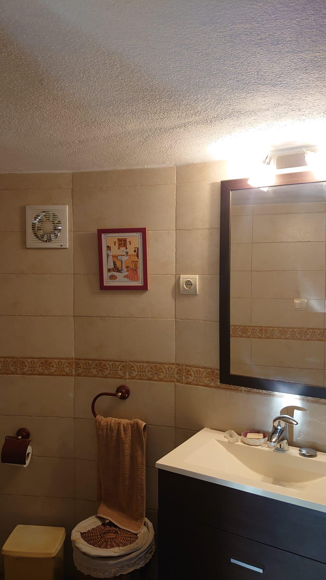 Bathroom featuring a dark wood vanity with white integrated sink, framed mirror with overhead lighting, and beige tiled walls with a decorative border.