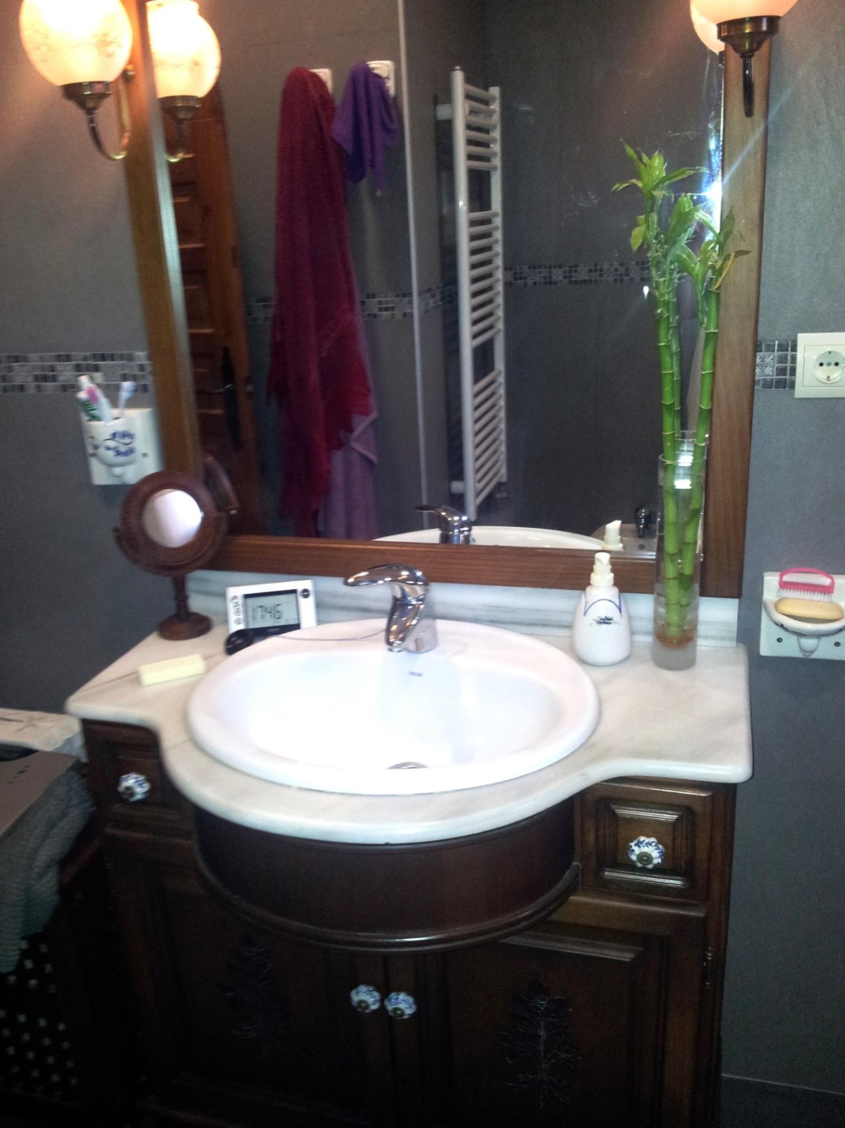 Bathroom featuring a marble countertop with an oval sink, a dark wood vanity with ceramic knobs, and a large framed mirror flanked by classic wall sconces.