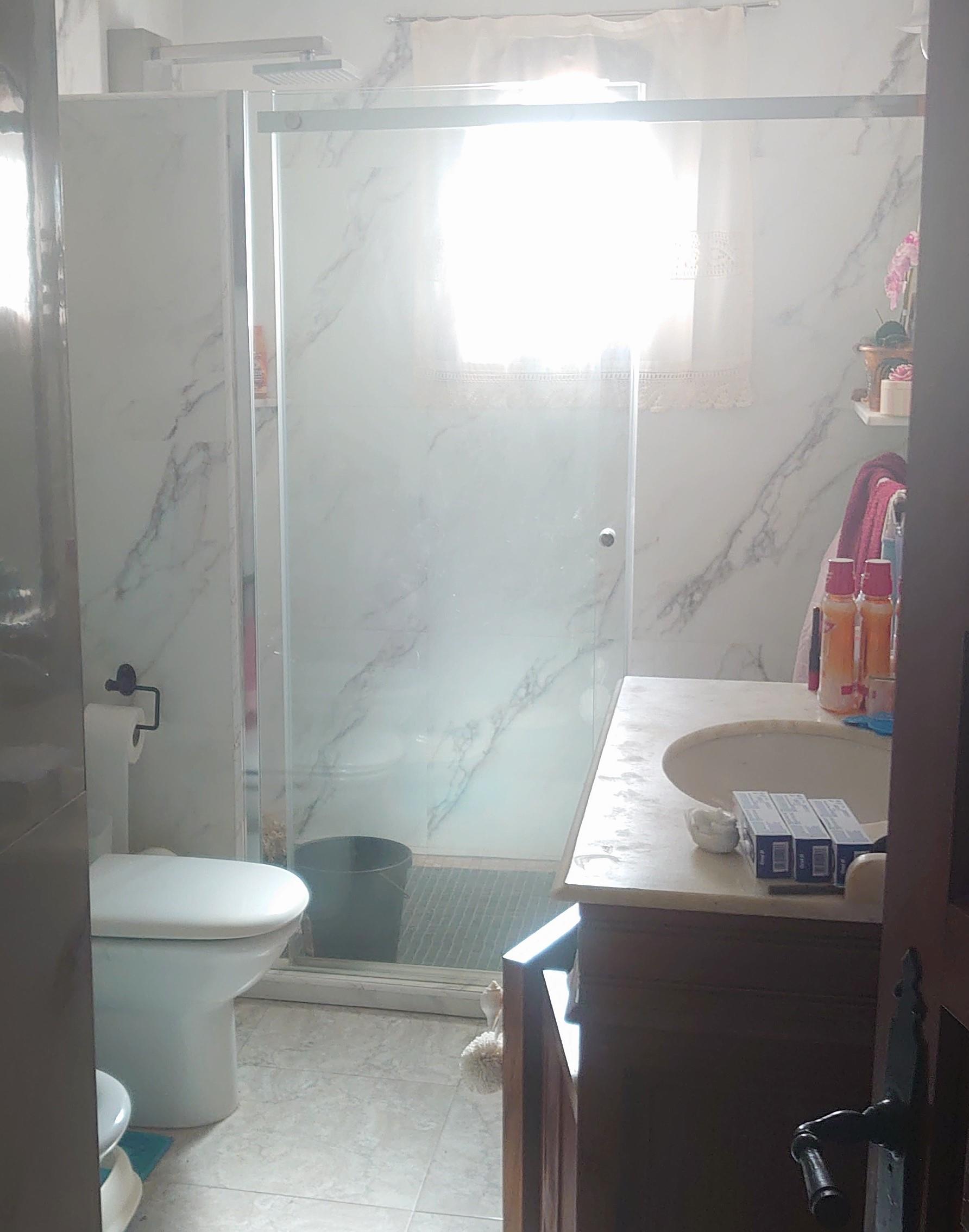 Bathroom featuring marble-effect wall tiles, a spacious walk-in shower with glass doors, and a wooden vanity with an integrated stone countertop.