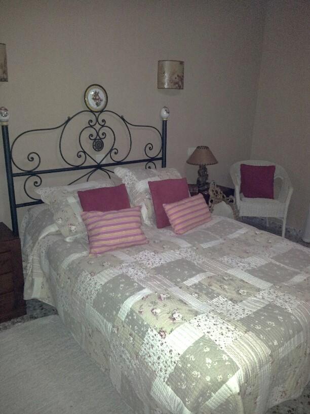 Bedroom featuring a wrought iron headboard, patchwork floral bedding, and pink accent pillows. A white wicker chair and classic wall sconces complete the space.