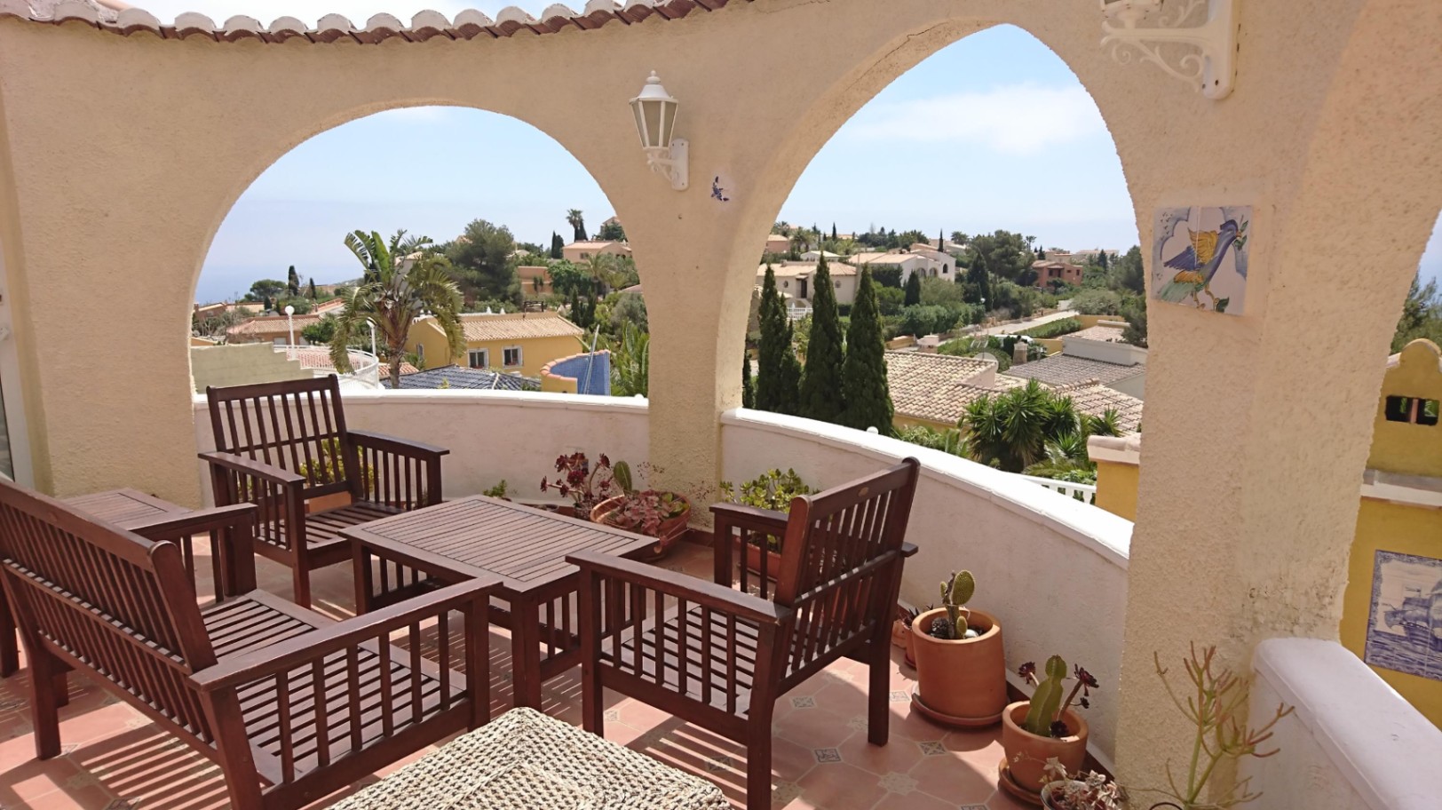 Circular terrace featuring Mediterranean arches, wooden seating, and elevated views of the sea and surrounding Cumbre del Sol landscape.