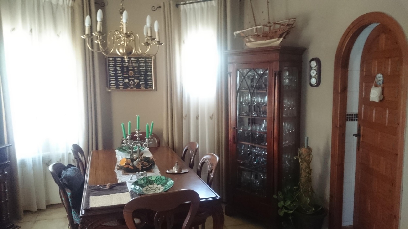 Classic dining area featuring a wooden table, a glass-fronted display cabinet, and a brass chandelier. An arched wooden doorway leads to the adjacent room.