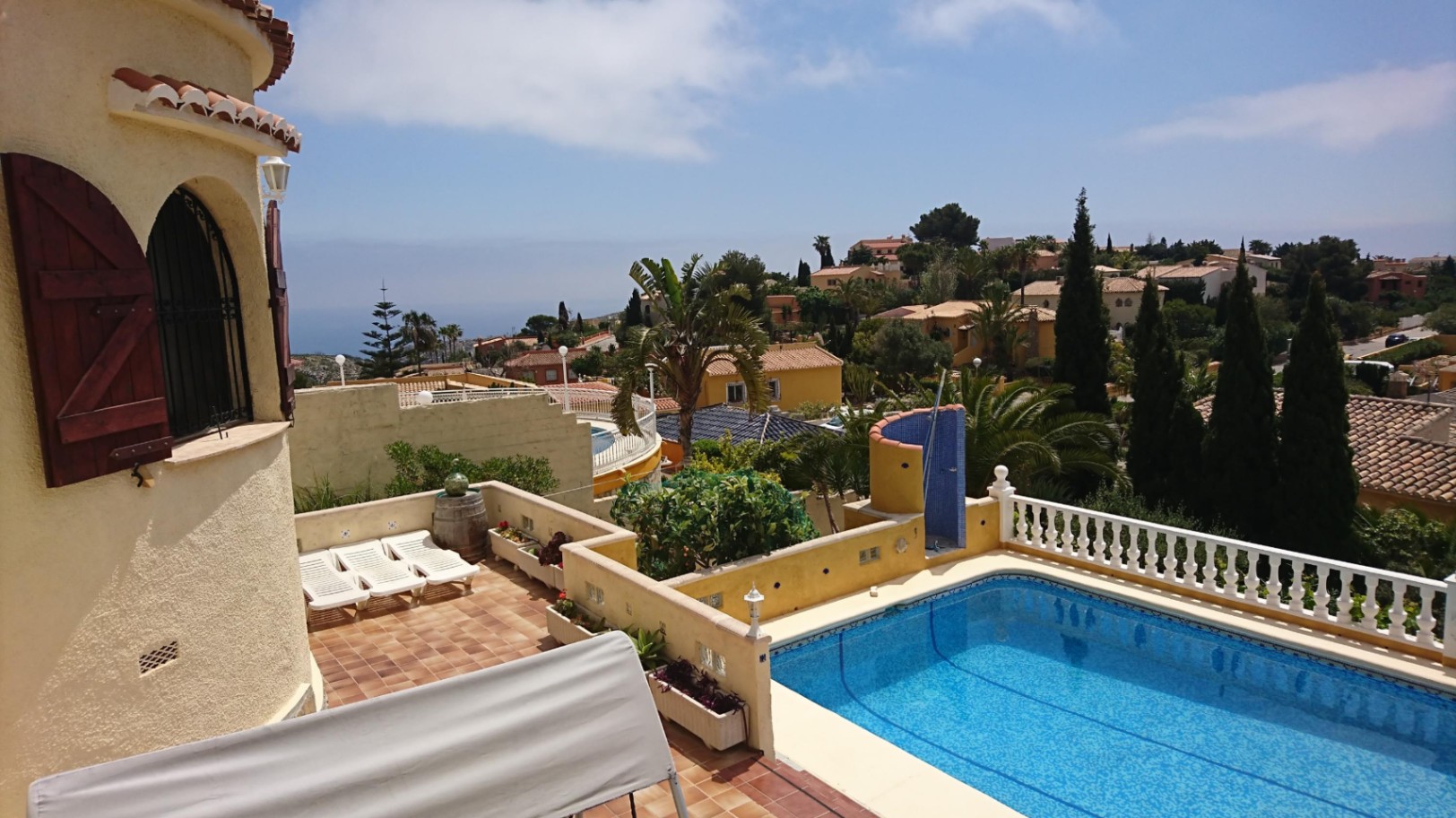 Exterior view of the rectangular swimming pool featuring a sun terrace, blue-tiled outdoor shower, and a traditional tower with wooden shutters.