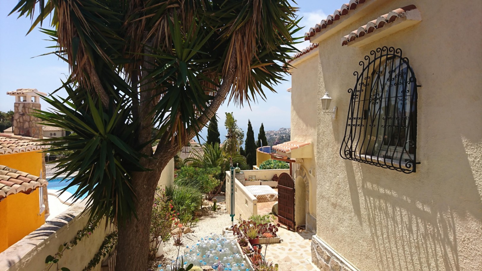 Exterior view of the villa featuring textured cream walls, a traditional wrought-iron window grille, and a Mediterranean garden with sea views.