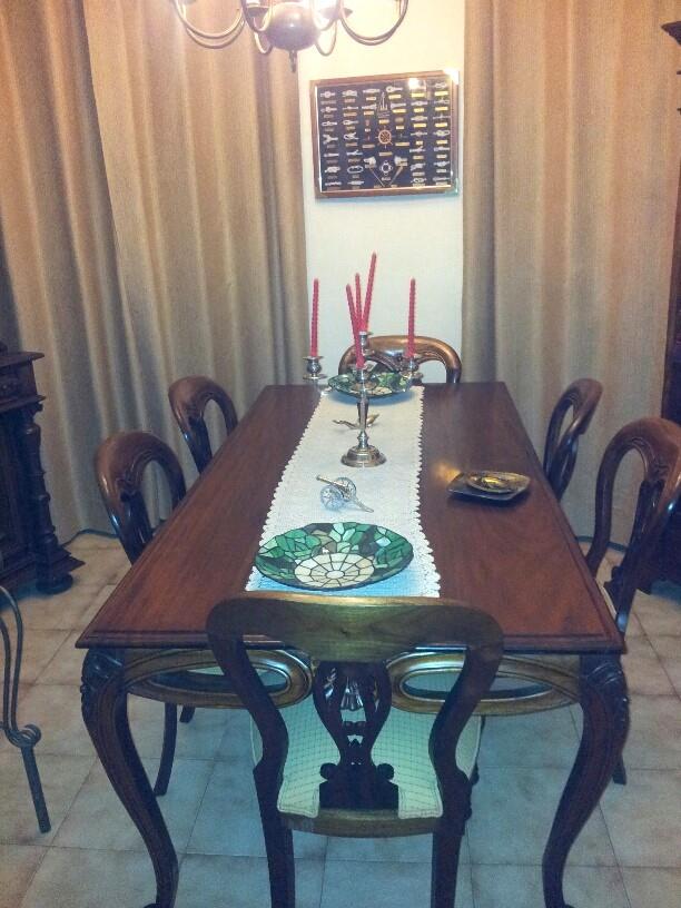 Formal dining area featuring a dark wood table with matching classical chairs, floor-to-ceiling beige curtains, and tiled flooring.