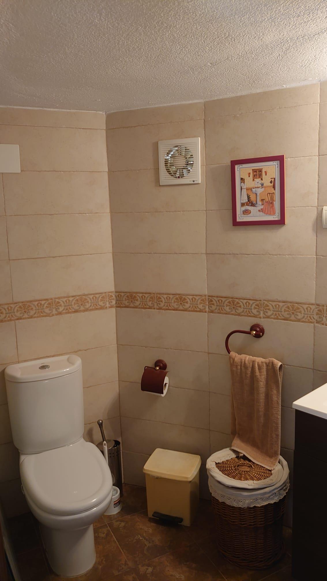 Functional bathroom with cream-toned tiling, an ornamental border, and white ceramic fixtures. Features dark wood accessories and a traditional wicker basket.