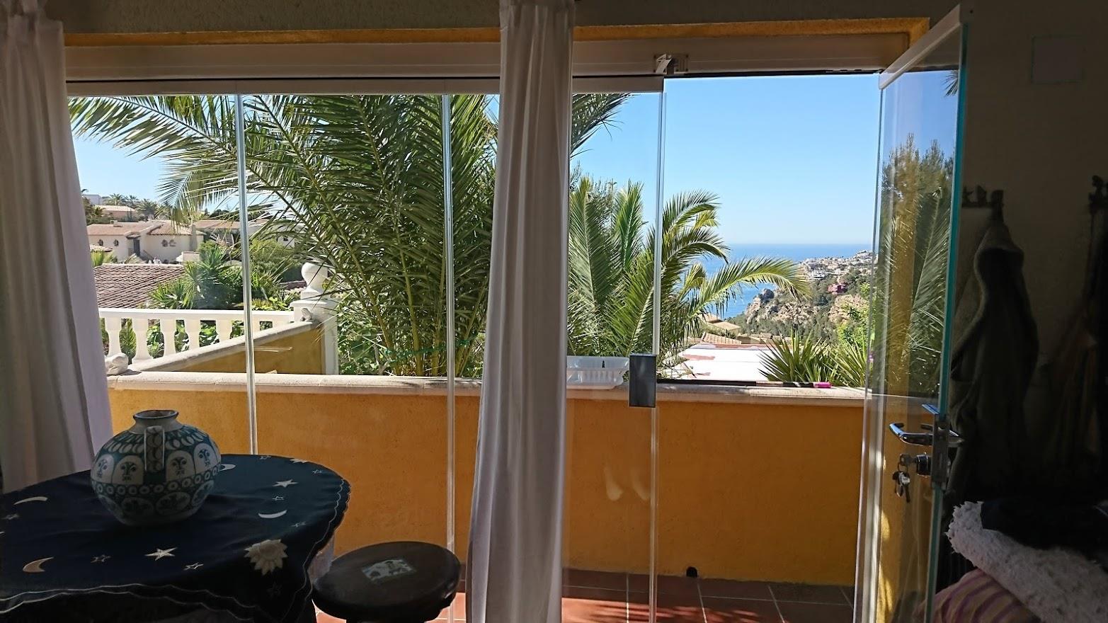 Glazed naya featuring glass curtains that open to sea views and palm trees. The interior space includes traditional tiling and abundant natural light.