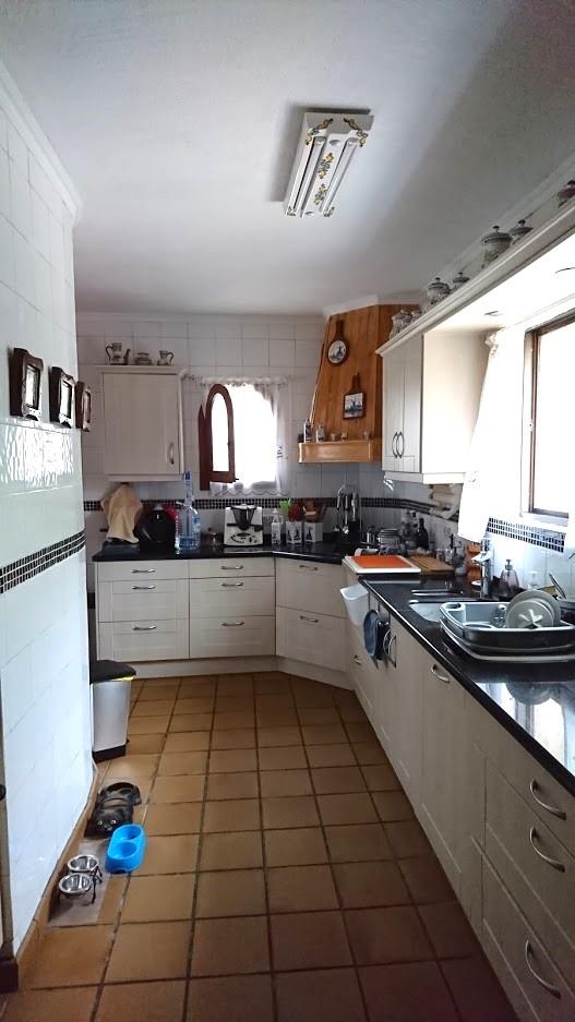 Independent kitchen with white cabinetry, dark granite countertops, and terracotta flooring. Features include a wooden range hood and ample natural light from the windows.