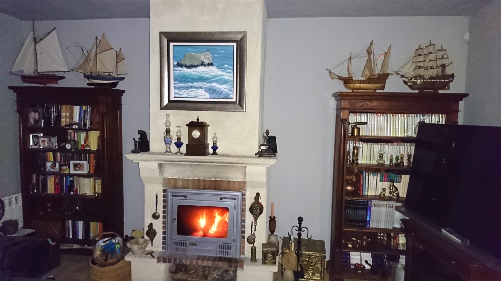 Living area featuring a stone fireplace with a modern wood-burning insert, framed by classic wooden bookshelves and nautical-themed decor.